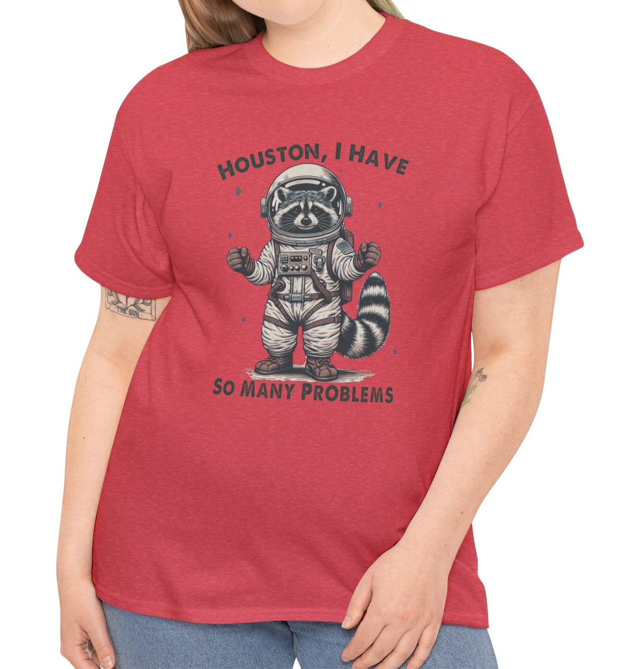 A person wearing a red T-shirt with an astronaut raccoon graphic and the text "Houston, I Have So Many Problems." Part of the Vivid Divergence Sensory Friendly Unisex Tees Range.