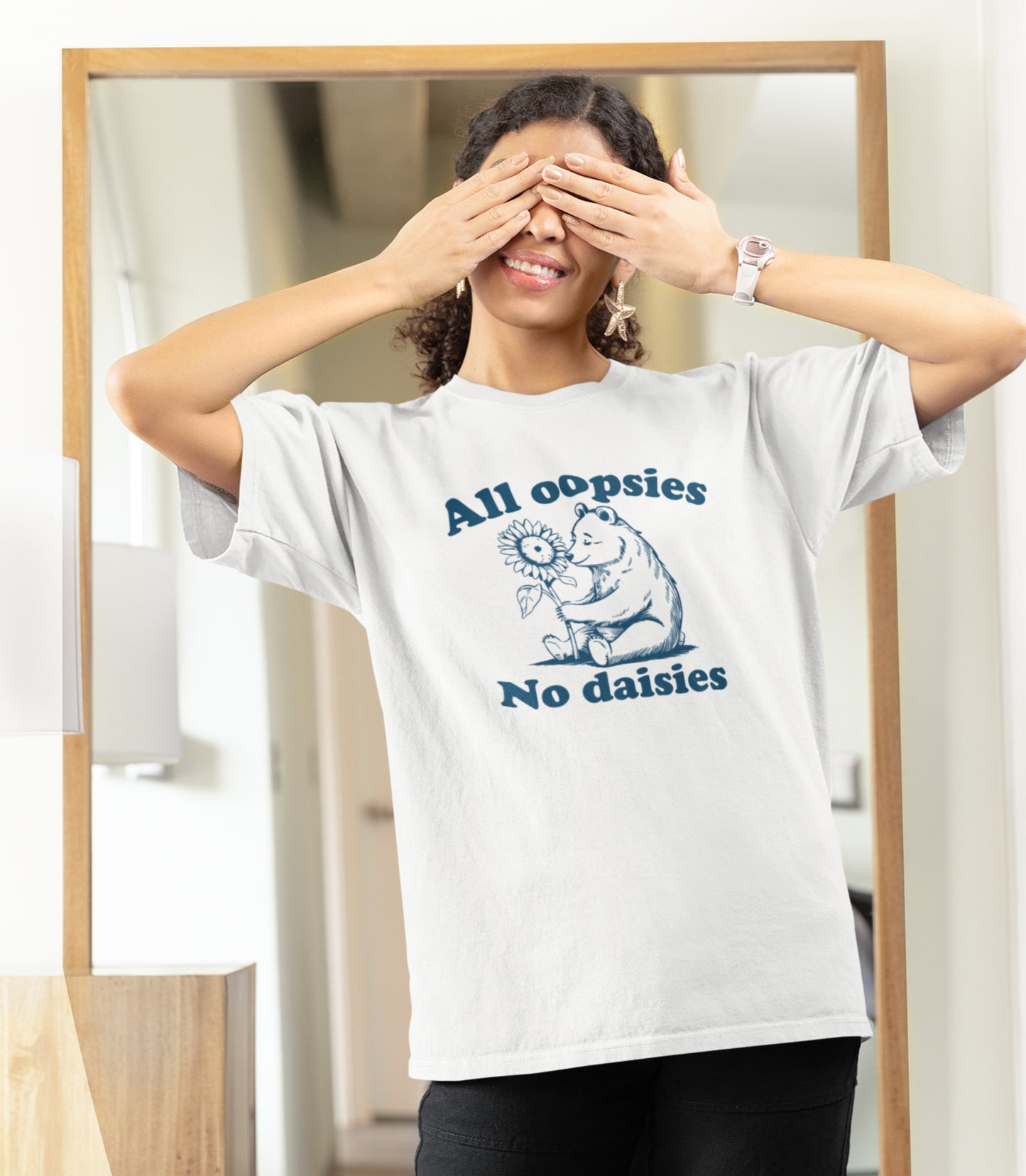 Model wearing a white T-shirt with "All oopsies, no daisies" and a playful bear graphic in blue text. Part of the Vivid Divergence Sensory Friendly Unisex Tees Range.