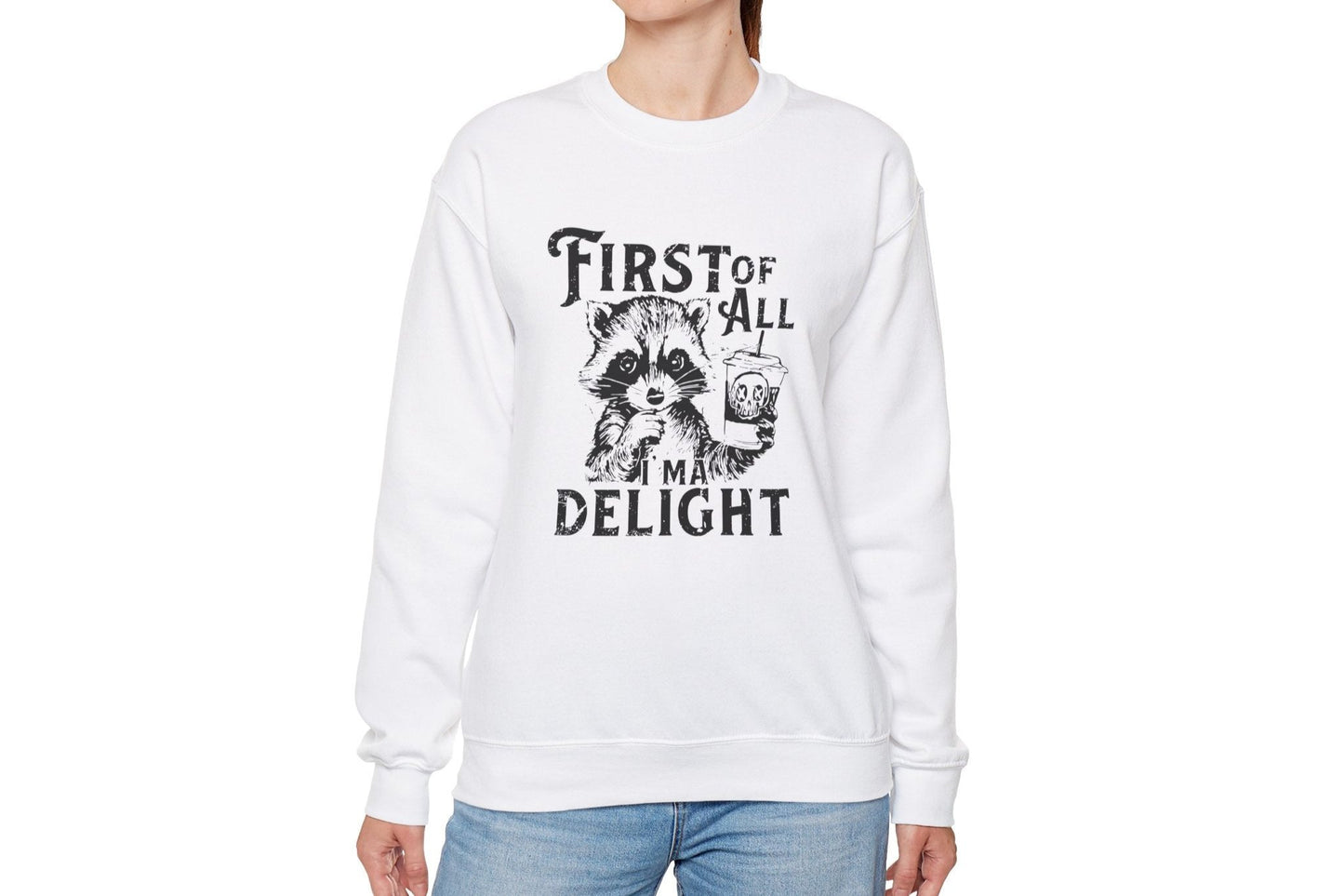 Model wearing a white sweater jumper with the text "First of All, I’m a Delight" and a cartoon raccoon illustration. Part of the Vivid Divergence Sensory Friendly Unisex Sweater Jumper Range.