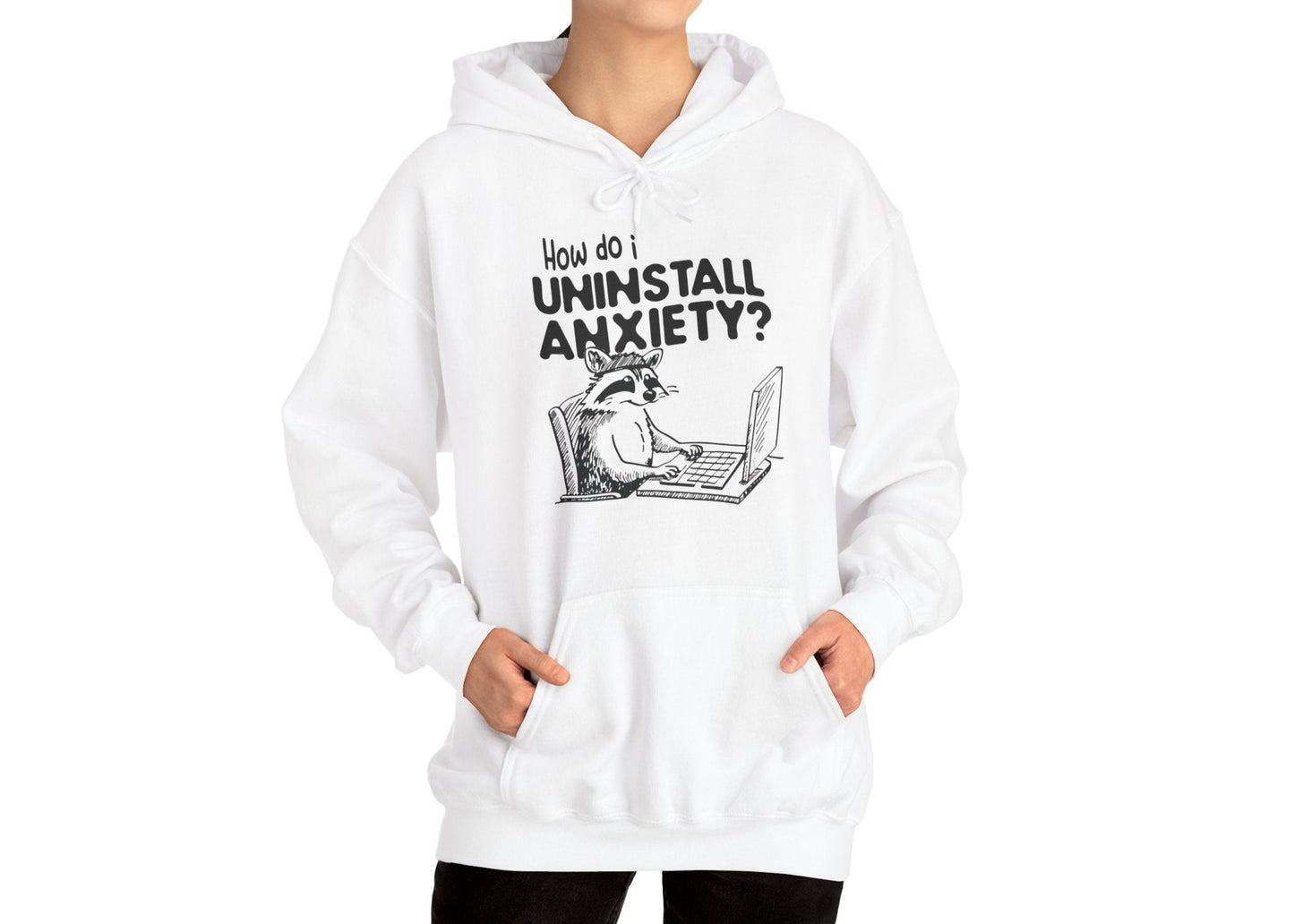 Model wearing a white hoodie featuring the text "How Do I Uninstall Anxiety?" and a cartoon illustration of a raccoon using a laptop. Part of the Vivid Divergence Sensory Friendly Unisex Hoodie Range.