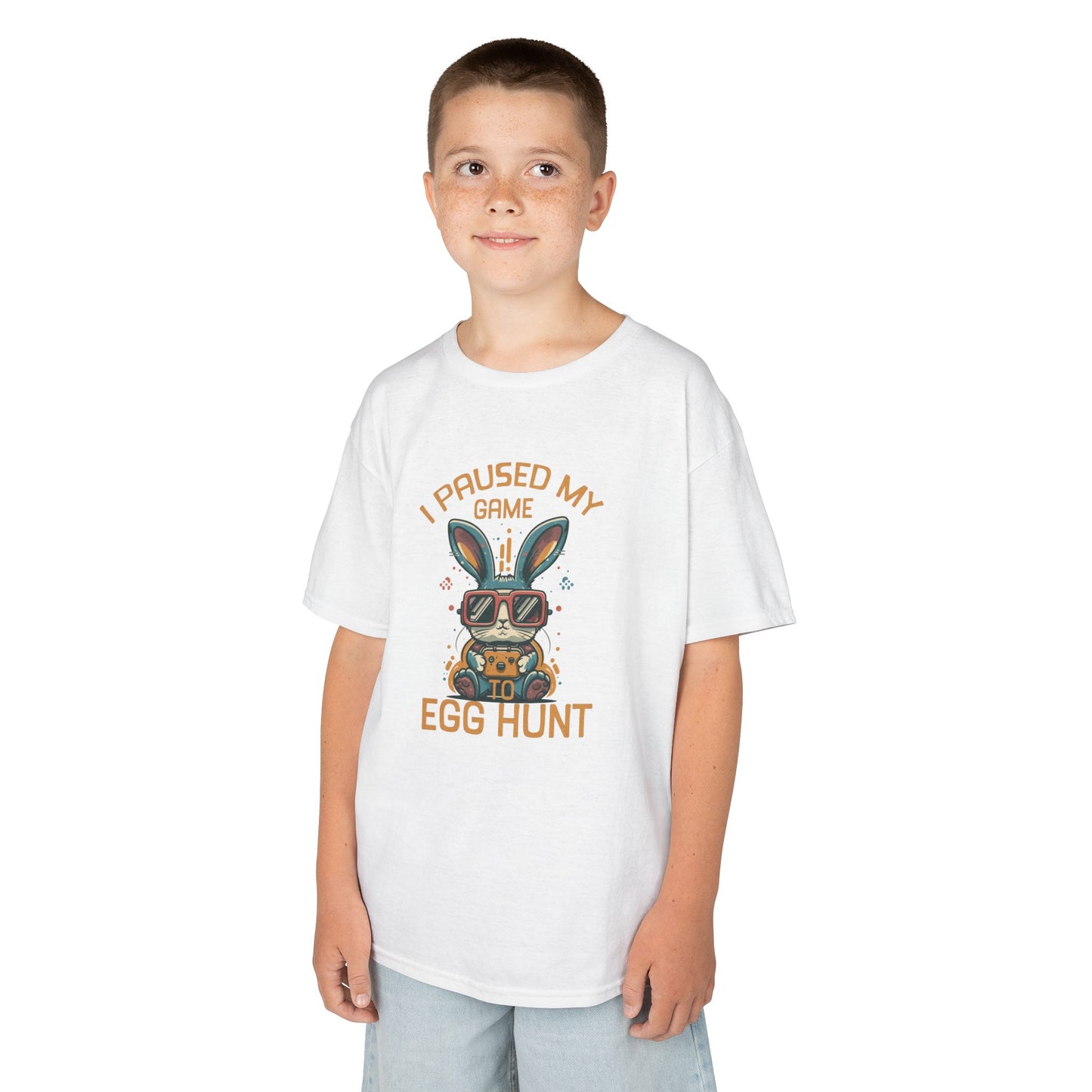 Child wearing a white Easter T-shirt featuring "I Paused My Game to Egg Hunt" with a gaming-inspired bunny, a cool choice for kids. Hop into the season in style and shop Easter shirts online today!