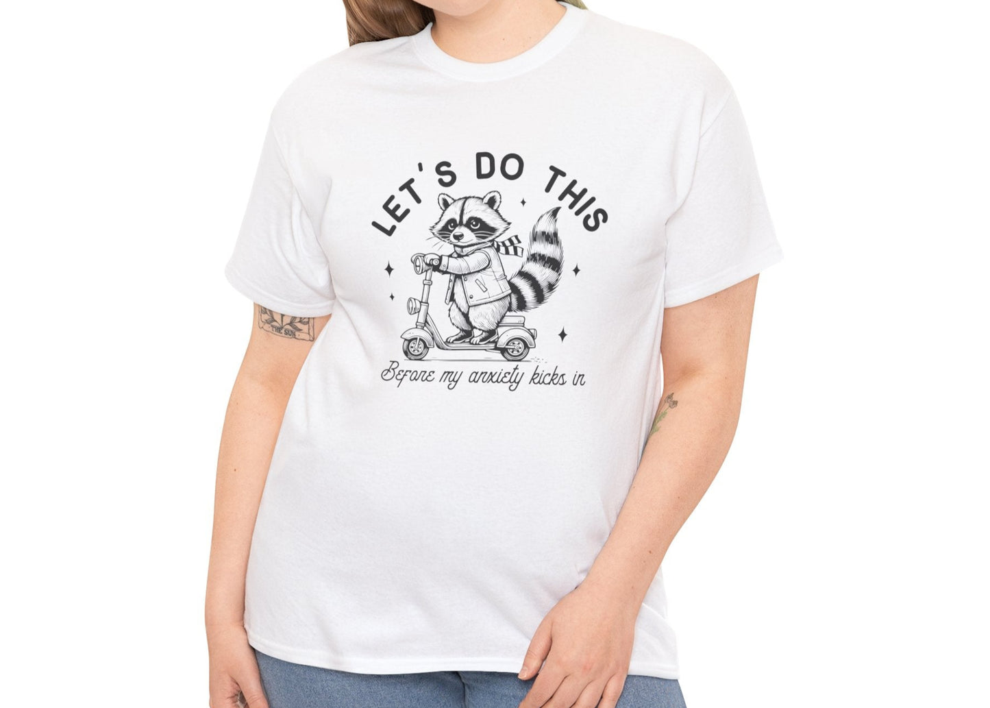 Model wearing a white T-shirt with "Let's Do This Before My Anxiety Kicks In" raccoon illustration and text, styled casually. Part of the Vivid Divergence Sensory Friendly Unisex Tees Range.