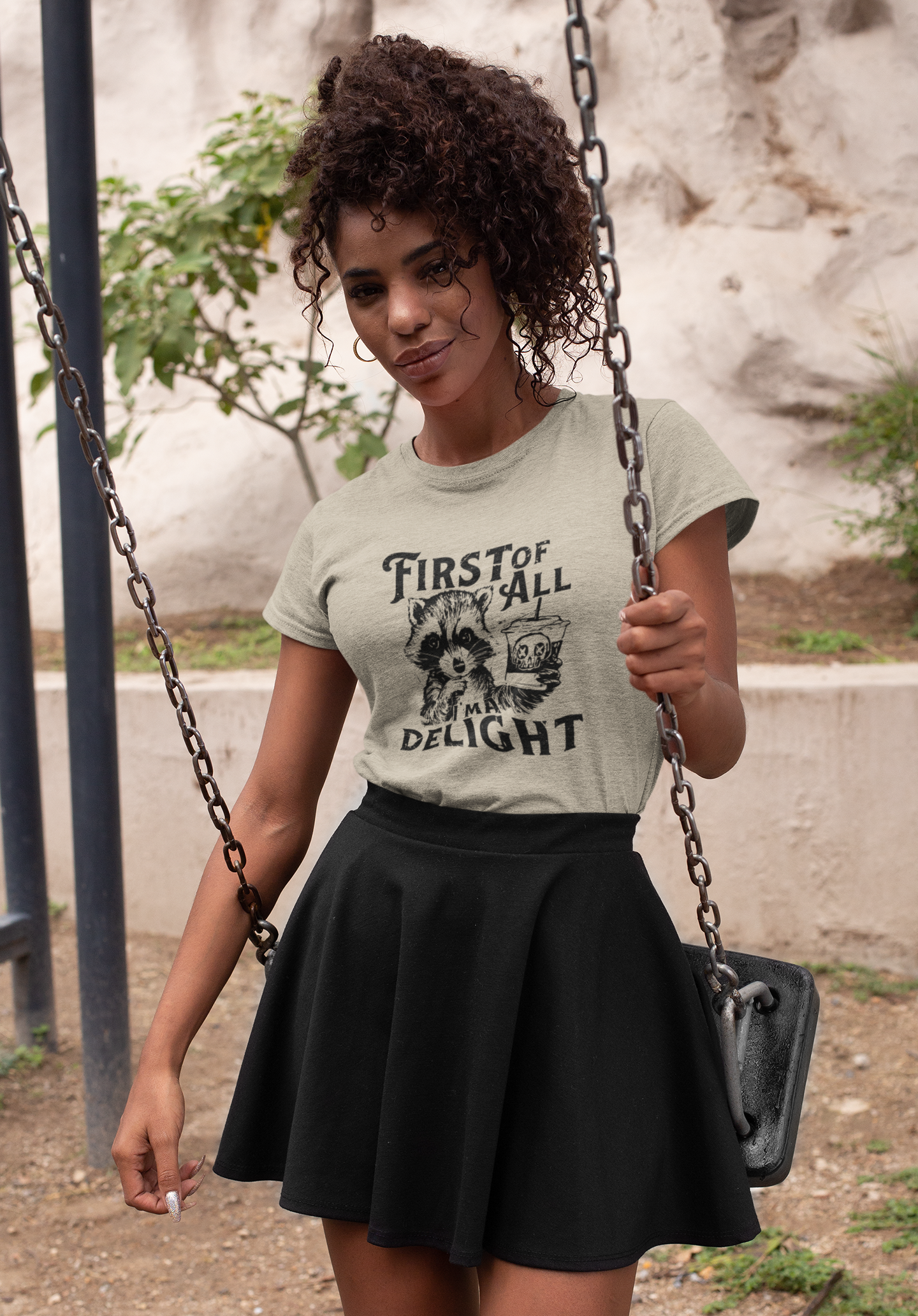 A woman wearing a white T-shirt with "First of All Delight" text and graphic design, paired with a black skirt, outdoor setting. Part of the Vivid Divergence Sensory Friendly Unisex Tees Range.