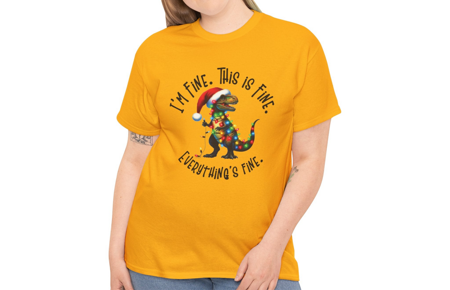 Model wearing an yellow T-shirt featuring a festive illustration of a dinosaur tangled in Christmas lights with the text "I’m Fine. This is Fine. Everything is Fine," styled casually. Part of the Vivid Divergence Sensory Friendly Unisex Tees Range.