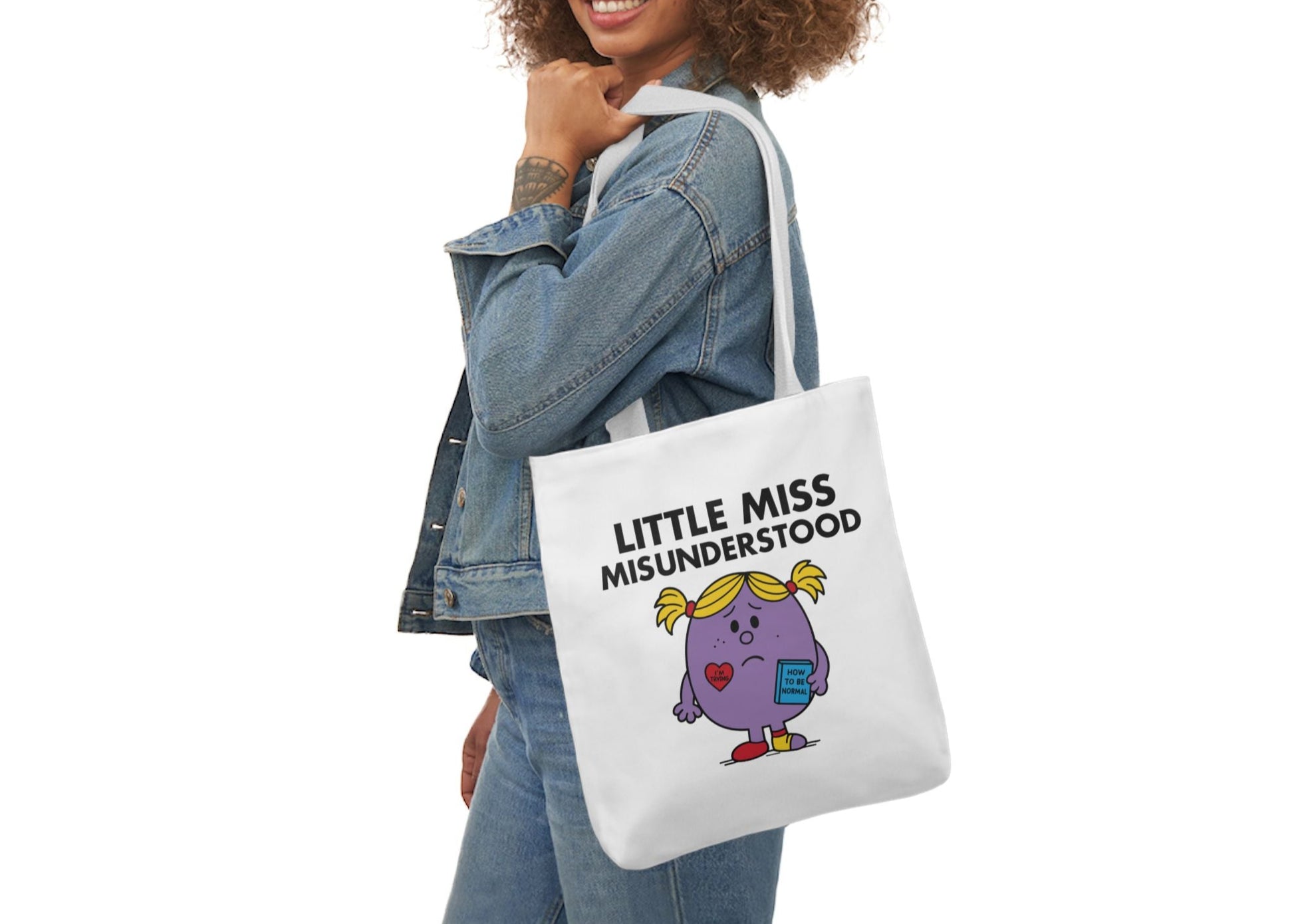 Woman in denim modeling the Little Miss Misunderstood tote bag over her shoulder. She’s soft, sensitive, and seriously misread the vibe. Part of the Vivid Divergence Little Miss Meme Collection!
