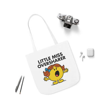 Flat lay of tote bag featuring Little Miss Oversharer surrounded by pens and earbuds. She’s already texting someone a three-paragraph life update. Part of the Vivid Divergence Little Miss Meme Collection!
