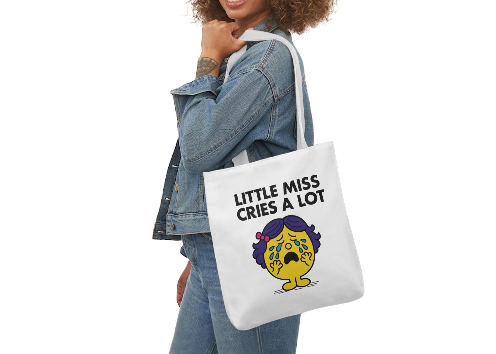 Woman in denim modeling the Little Miss Cries A Lot tote bag over her shoulder. She's powered by caffeine and emotional spiral. Part of the Vivid Divergence Little Miss Meme Collection!

