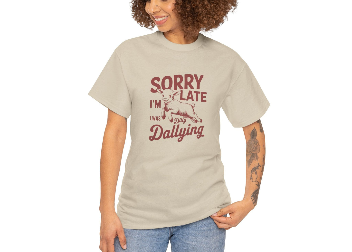 Woman in beige T-shirt with “Sorry I’m Late I Was Dilly Dallying” text, standing with hands in pockets. Running late, looking cute. Part of the Vivid Divergence Memewear Collection!
