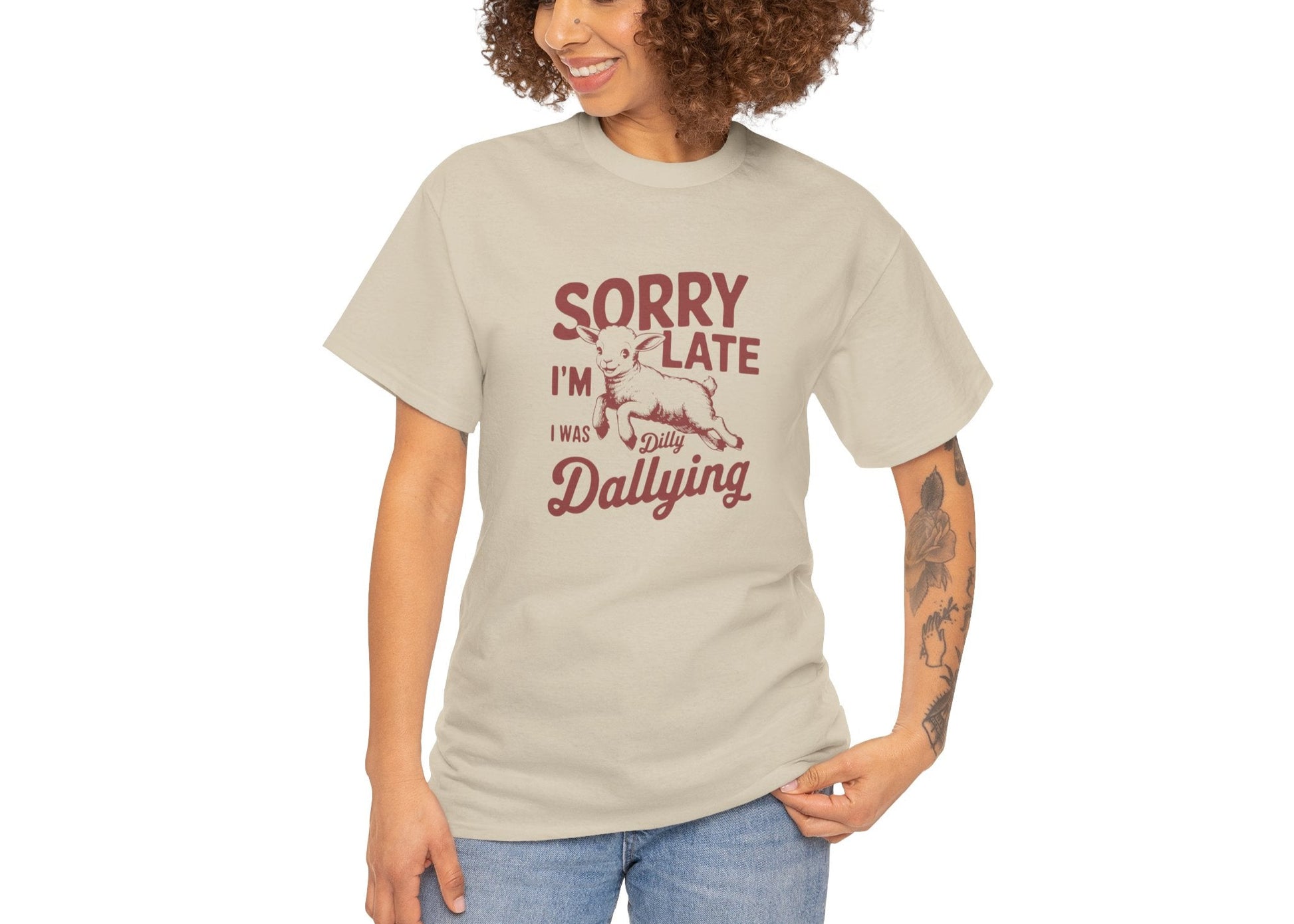 Woman in beige T-shirt with “Sorry I’m Late I Was Dilly Dallying” text, standing with hands in pockets. Running late, looking cute. Part of the Vivid Divergence Memewear Collection!

