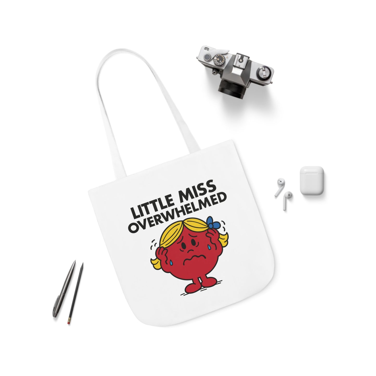 Flat lay of tote bag featuring Little Miss Overwhelmed surrounded by pens and earbuds. The tote may be calm, but her brain is not. Part of the Vivid Divergence Little Miss Meme Collection!
