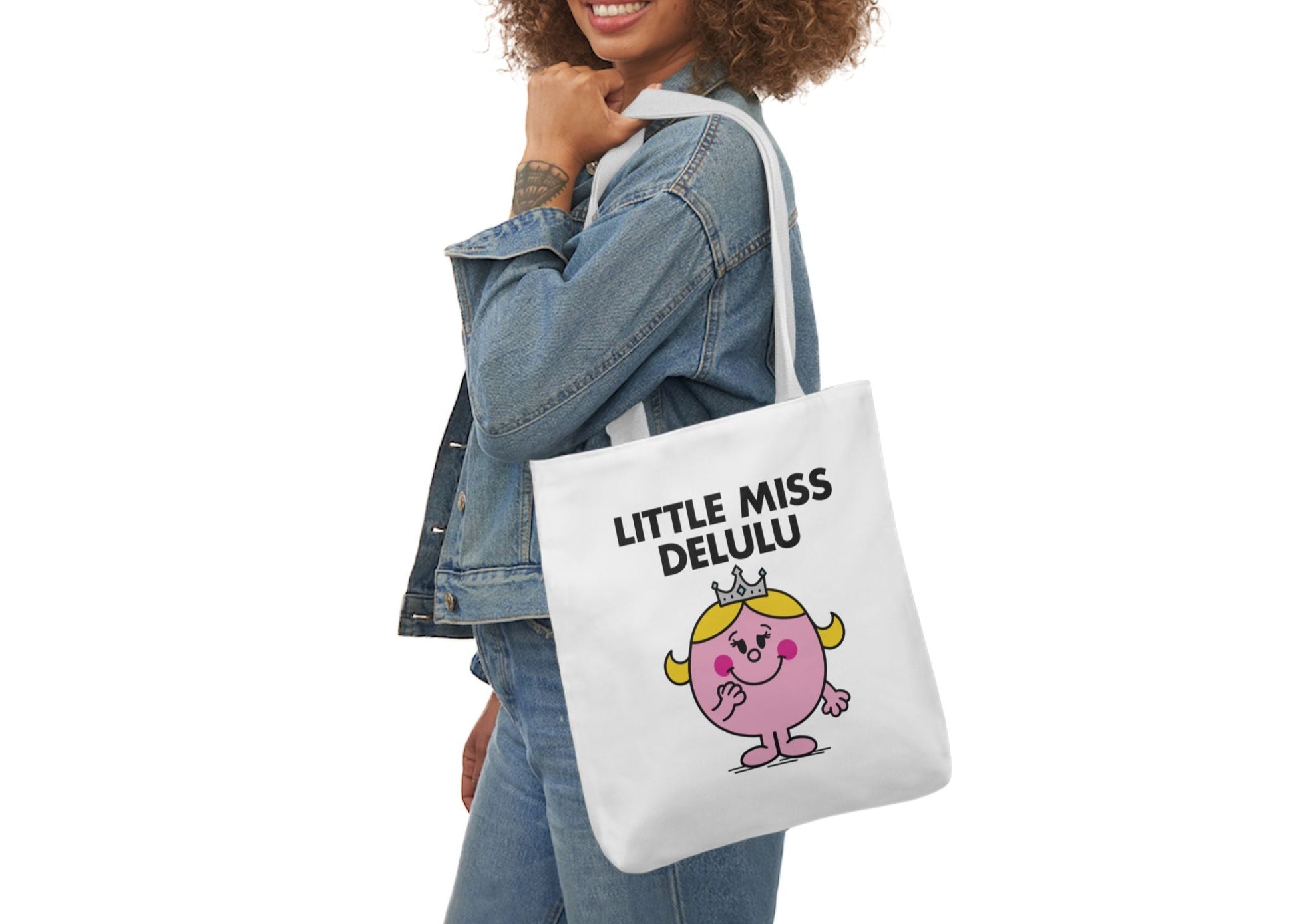 Woman in denim smiling while wearing the Little Miss Delulu tote over her shoulder. She’s off to manifest a whole relationship from eye contact. Part of the Vivid Divergence Little Miss Meme Collection!
