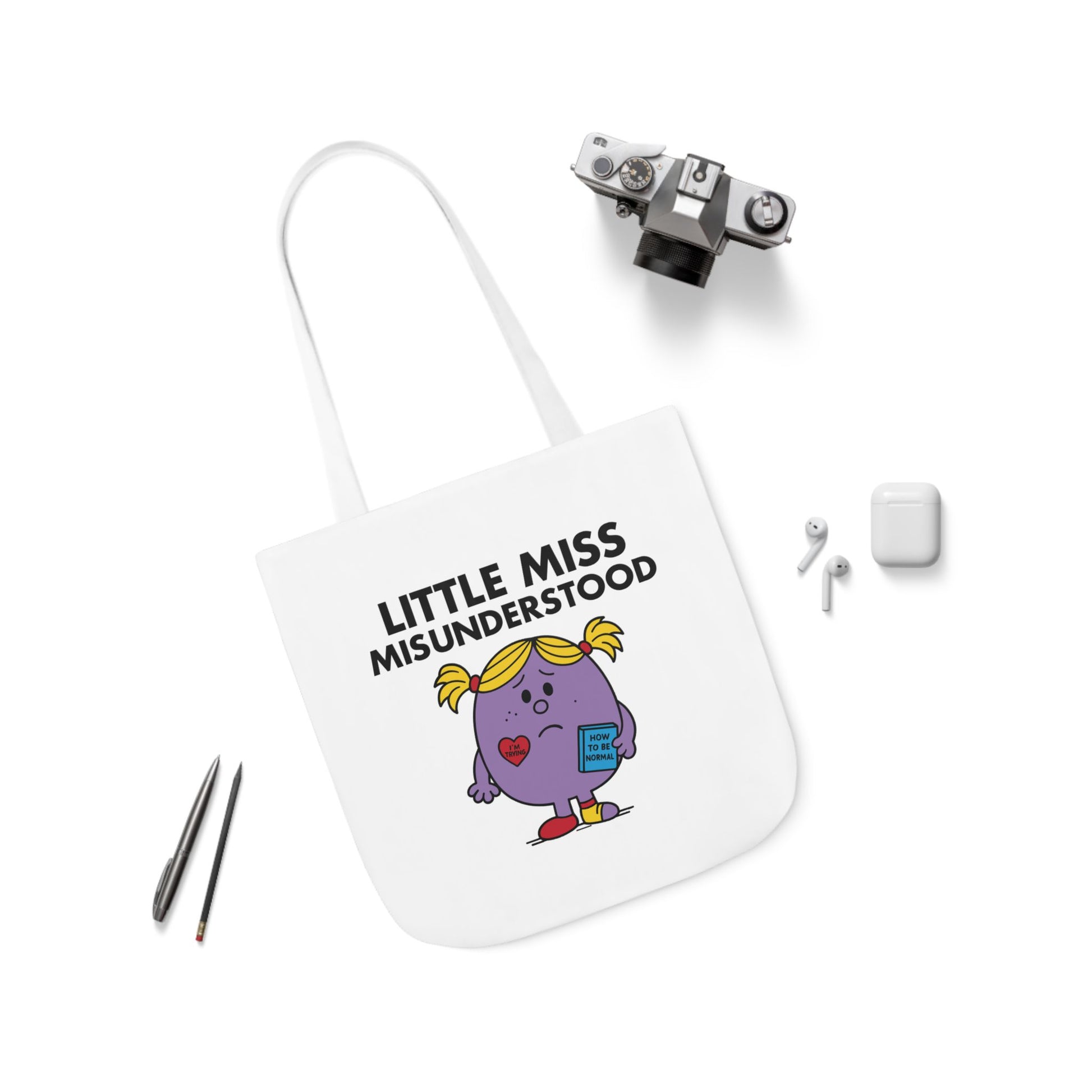 Flat lay of tote bag showing Little Miss Misunderstood surrounded by accessories. She replayed the convo for hours wondering what went wrong. Part of the Vivid Divergence Little Miss Meme Collection!
