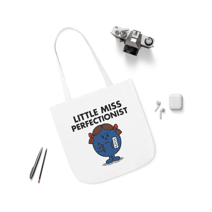 Flat lay of tote bag featuring Little Miss Perfectionist surrounded by accessories. She reorganized her entire workspace instead of starting the task. Part of the Vivid Divergence Little Miss Meme Collection!
