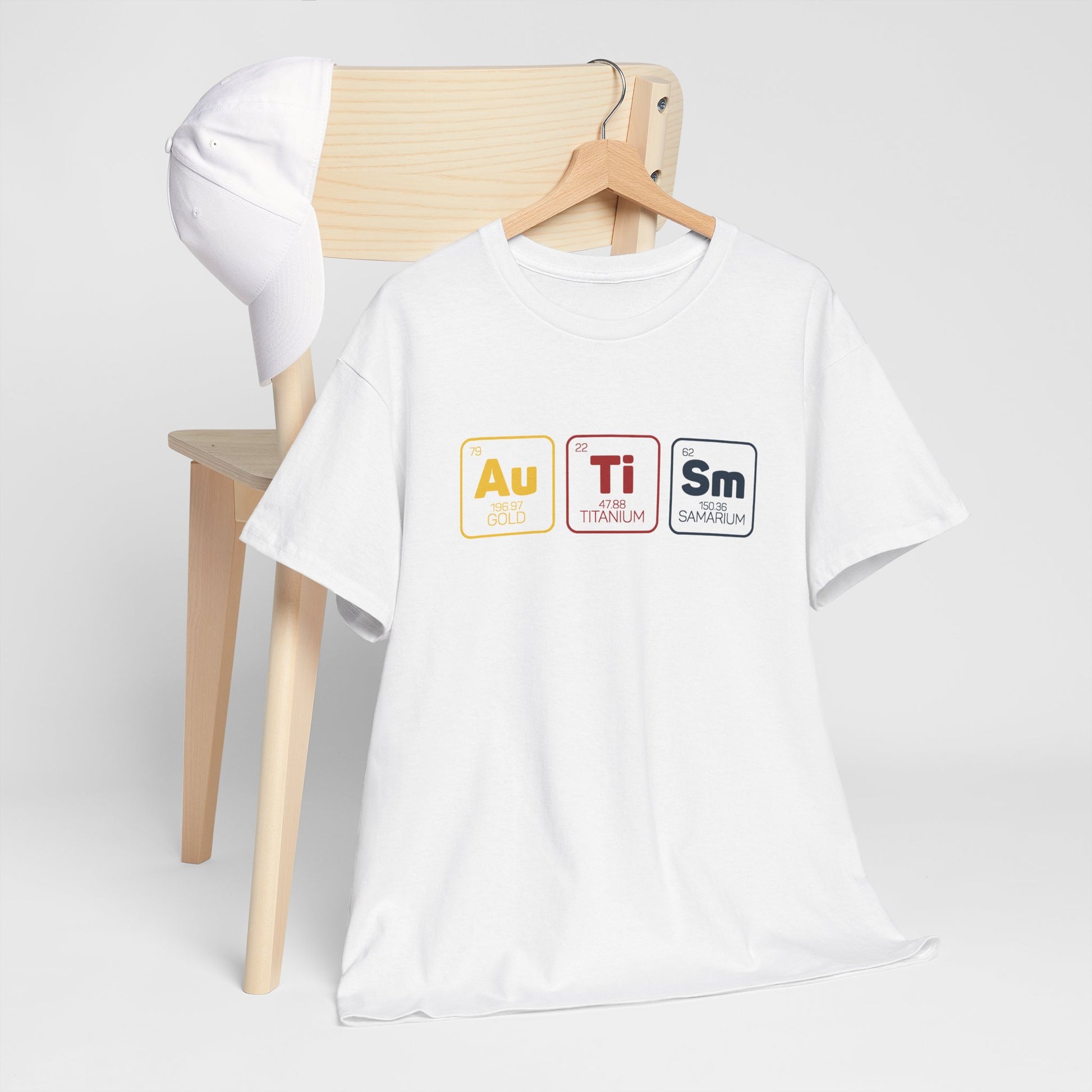 White "Au Ti Sm" periodic table Autism T-shirt draped over a wooden chair. Part of the Vivid Divergence Sensory Friendly Unisex Tees Range.