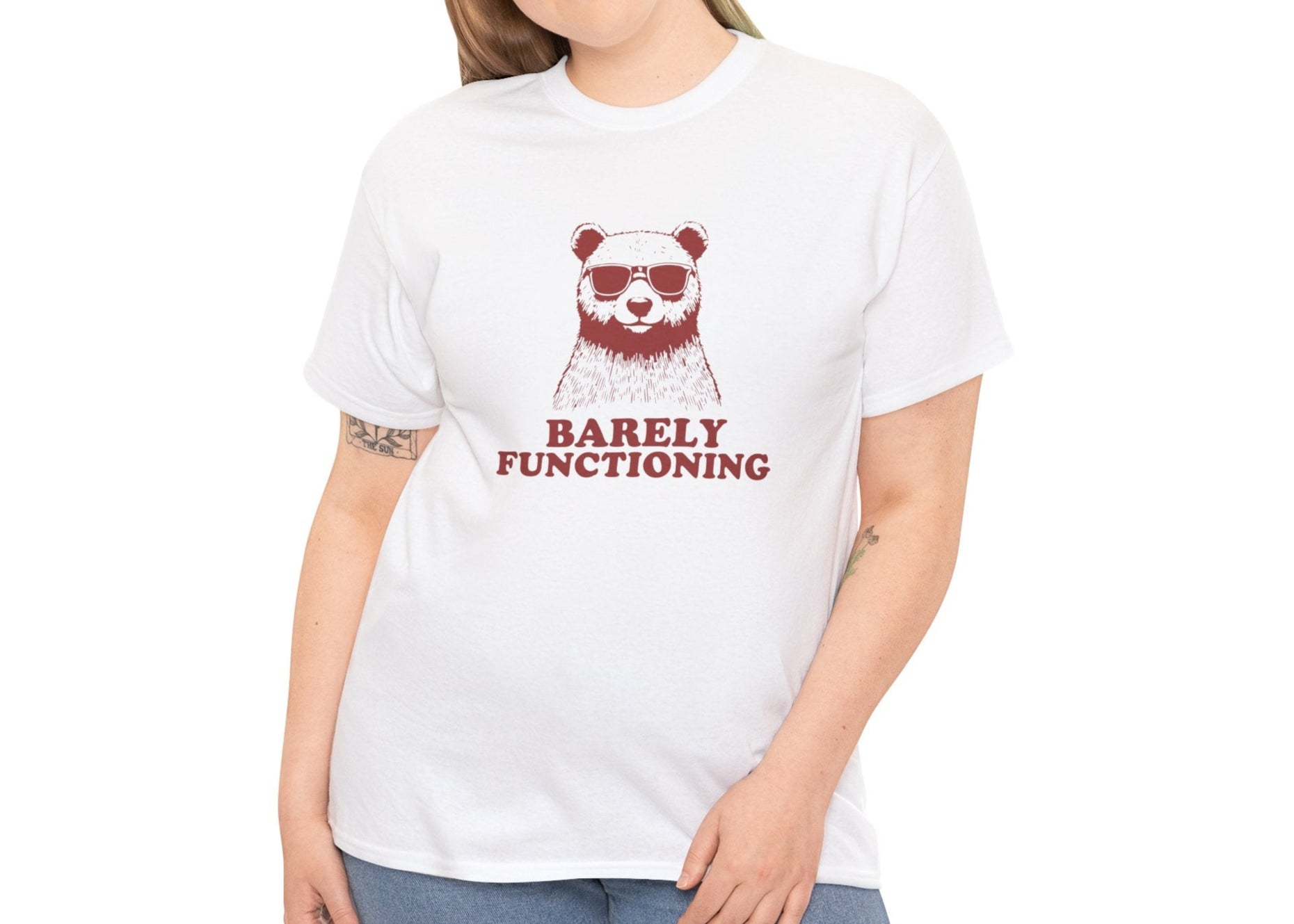 Female model wearing a white T-shirt with a red bear graphic and "Barely Functioning" text. Part of the Vivid Divergence Sensory Friendly Unisex Tees Range.