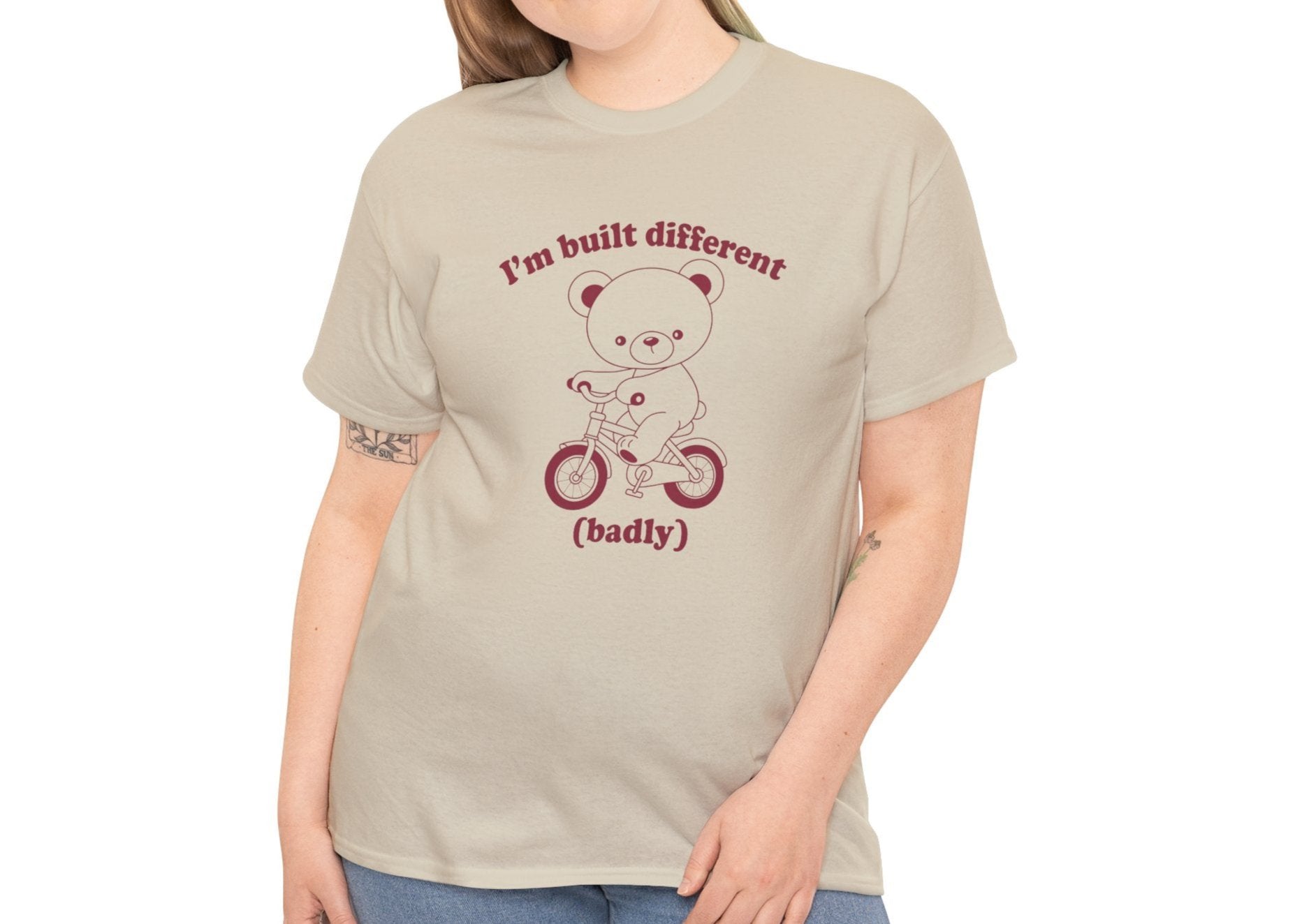 Model wearing a beige T-shirt with the "Built Different (Badly)" bear design. Part of the Vivid Divergence Sensory Friendly Unisex Tees Range.