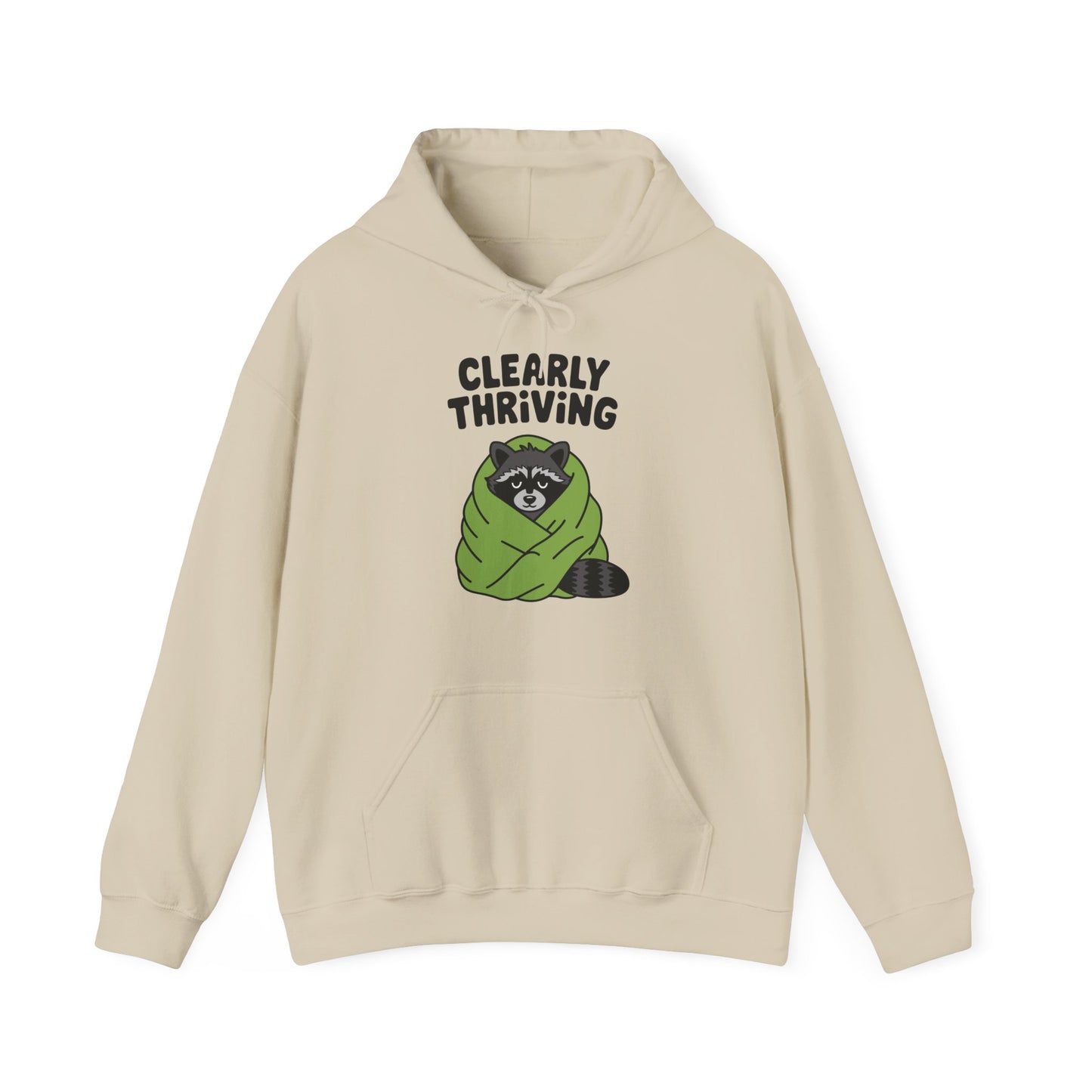 Front view of a beige hoodie featuring the text "Clearly Thriving" and a cartoon illustration of a raccoon wrapped in a cozy blanket. Part of the Vivid Divergence Sensory Friendly Unisex Hoodie Range.