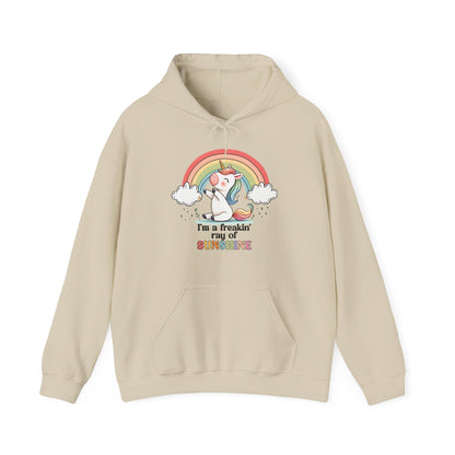 Front view of a beige hoodie featuring a grumpy-looking unicorn with wings under a rainbow, with the text "I'm a Freakin' Ray of Sunshine." Part of the Vivid Divergence Sensory Friendly Unisex Hoodie Range.