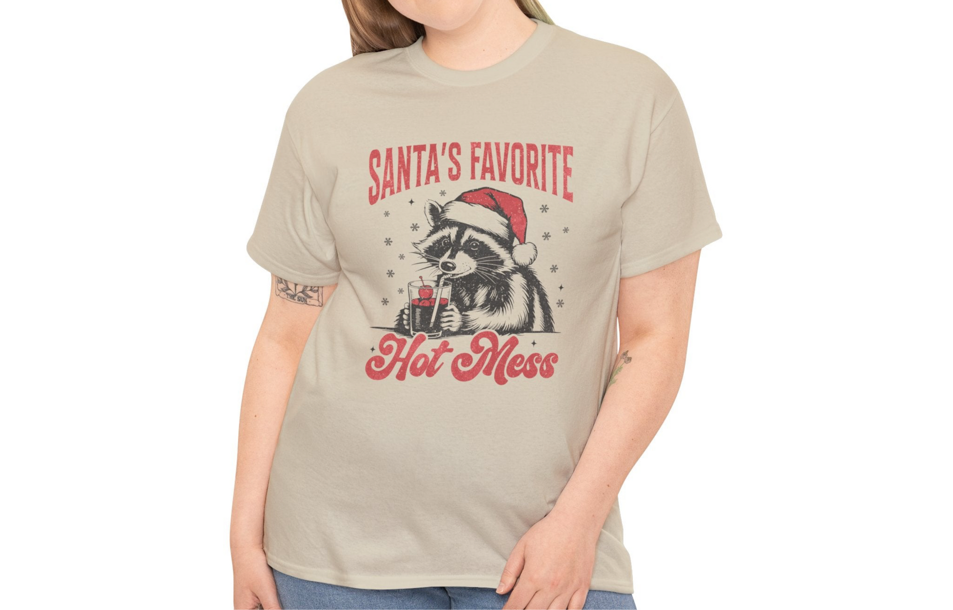 Model wearing a beige T-shirt featuring a "Santa's Favorite Hot Mess" design with a festive raccoon wearing a Santa hat. Part of the Vivid Divergence Sensory Friendly Unisex Tees Range. 