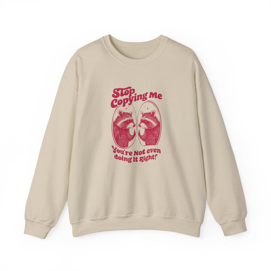 Front view of a beige sweater jumper with the text "Stop Copying Me, You’re Not Even Doing It Right," featuring a cartoon raccoon looking in a mirror. Part of the Vivid Divergence Sensory Friendly Unisex Sweater Jumper Range.