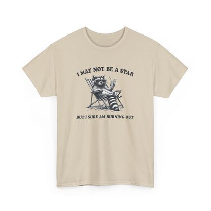 Hanging front view of a beige T-shirt featuring a cute raccoon holding a star with text that reads "I May Not Be A Star, But I Sure Am Burning Out." Part of the Vivid Divergence Sensory Friendly Unisex Tees Range.