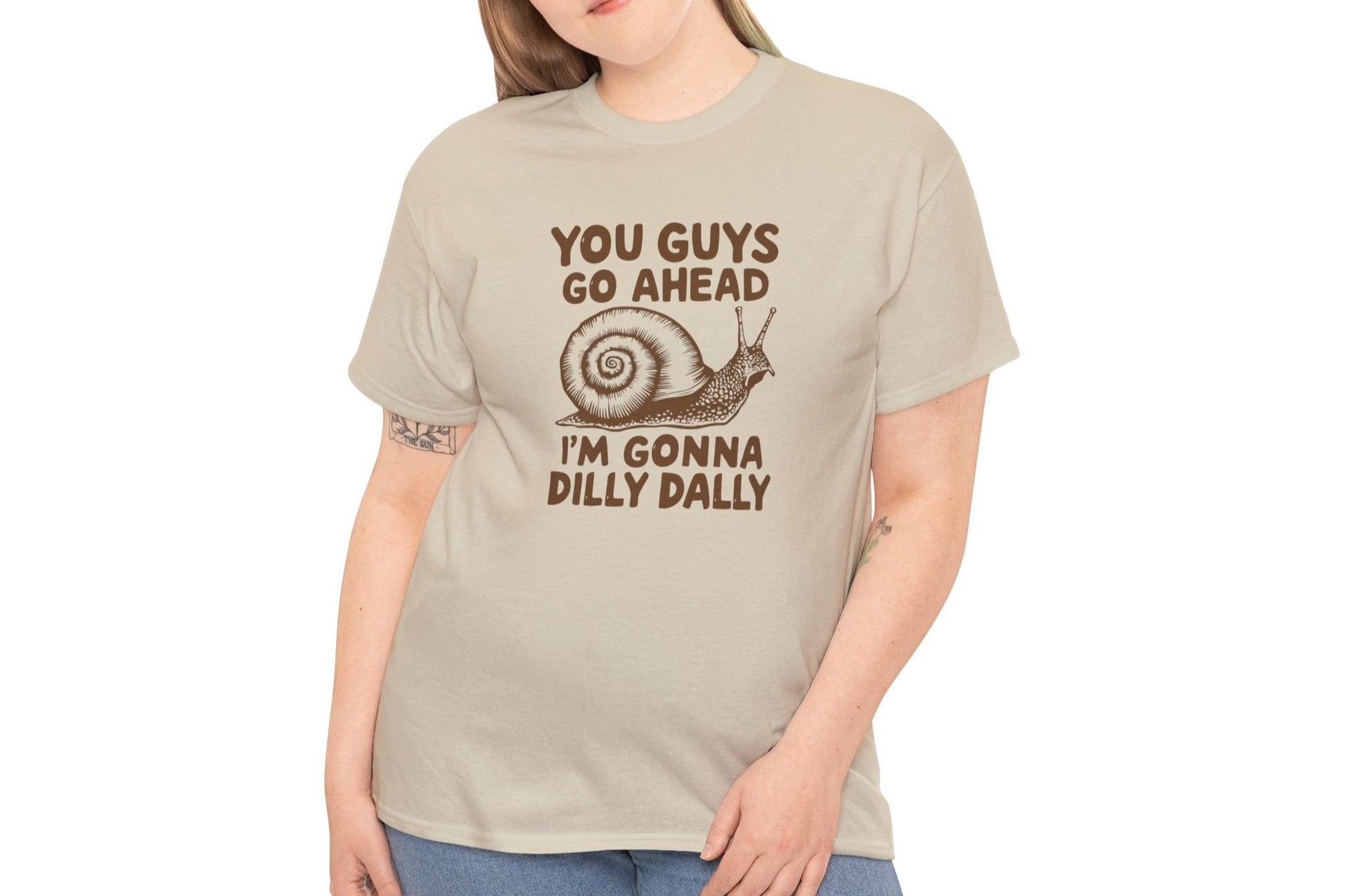 Model wearing a beige T-shirt with the text "You Guys Go Ahead, I'm Gonna Dilly Dally" and a playful snail graphic in brown. Part of the Vivid Divergence Sensory Friendly Unisex Tees Range.