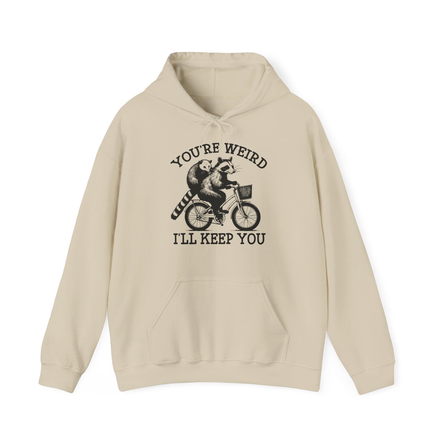 Front view of a beige hoodie featuring the text "You're Weird, I'll Keep You" with a cartoon illustration of two raccoons riding a bicycle. Part of the Vivid Divergence Sensory Friendly Unisex Hoodie Range.