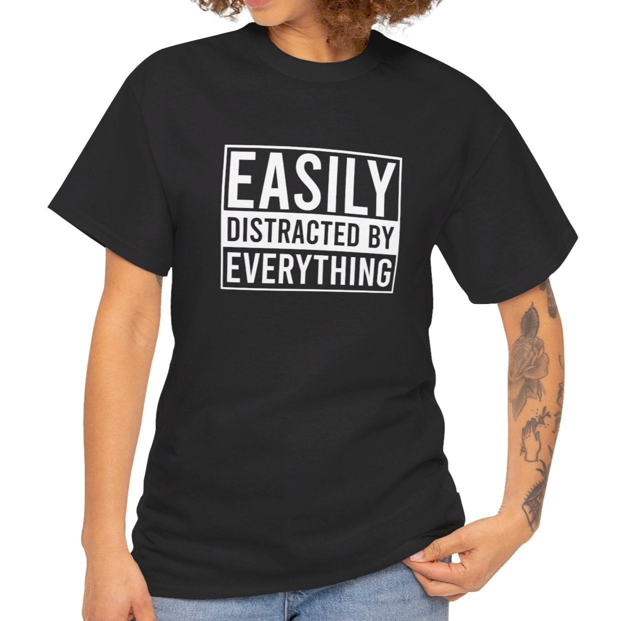 A person wearing a black T-shirt with "Easily Distracted by Everything" text, shown in a casual standing pose. Part of the Vivid Divergence Sensory Friendly Unisex Tees Range.