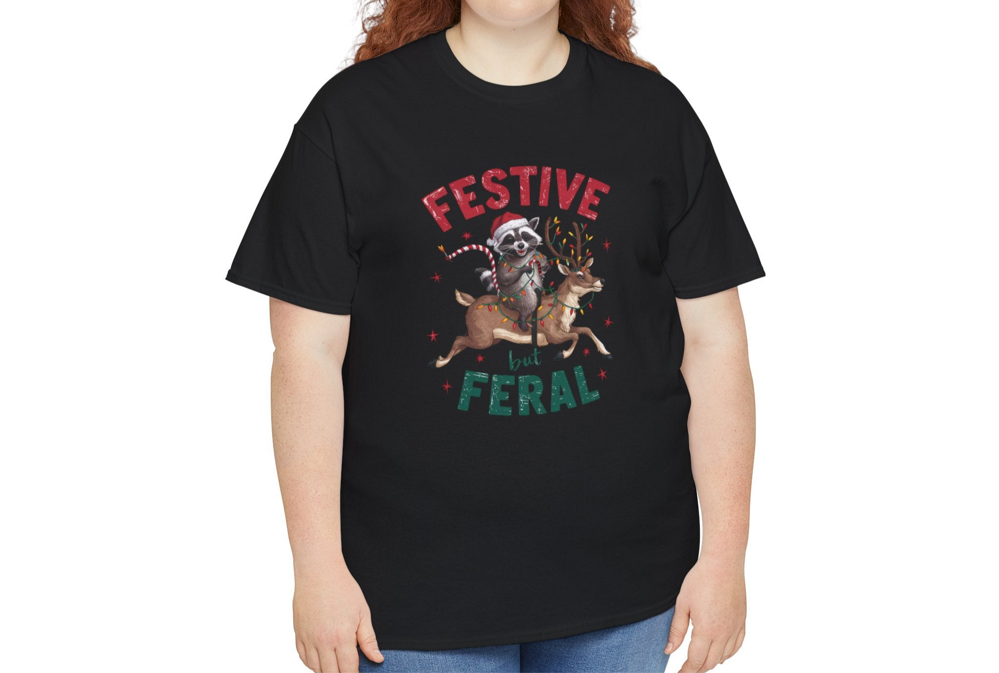 Model wearing a black T-shirt featuring a festive raccoon holding Christmas lights and the text "Festive but Feral," paired with casual jeans. Part of the Vivid Divergence Sensory Friendly Unisex Tees Range.