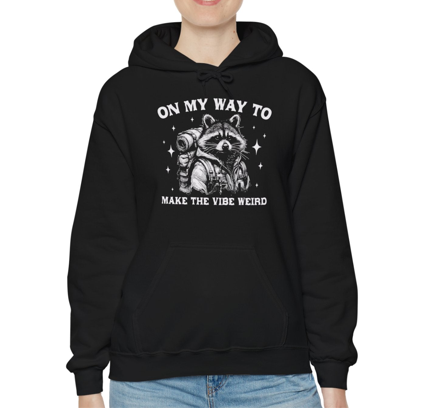 Model wearing a black hoodie featuring the text "On My Way to Make the Vibe Weird" and a cartoon illustration of a raccoon holding a stick. Part of the Vivid Divergence Sensory Friendly Unisex Hoodie Range.