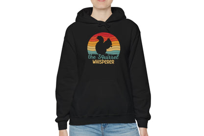 Model wearing a black hoodie featuring the text "Squirrel Whisperer" with an ADHD mascot design of a squirrel and a retro sunset background. Part of the Vivid Divergence Sensory Friendly Unisex Hoodie Range.