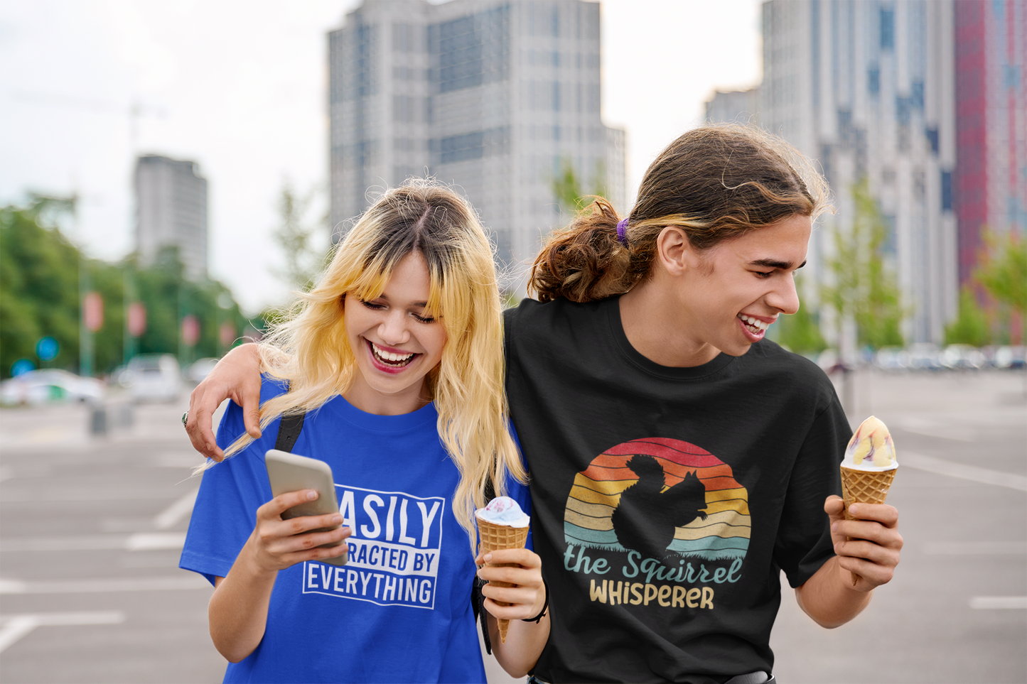 Model sitting outdoors wearing a black T-shirt with "The Squirrel Whisperer" and a silhouette of a squirrel against a retro sunset design. Part of the Vivid Divergence Sensory Friendly Unisex Tees Range.