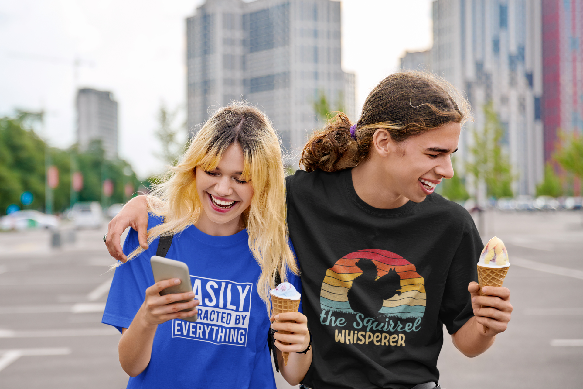 Model sitting outdoors wearing a black T-shirt with "The Squirrel Whisperer" and a silhouette of a squirrel against a retro sunset design. Part of the Vivid Divergence Sensory Friendly Unisex Tees Range.