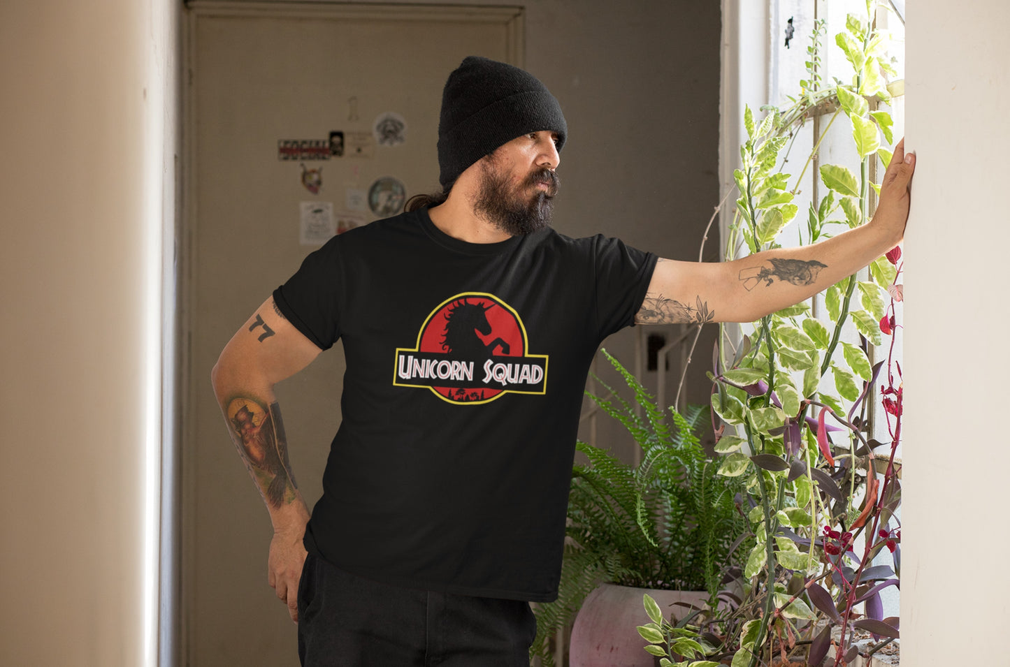 Model wearing a black T-shirt with "Unicorn Squad" in bold white text inside a red and yellow Jurassic Park-style logo featuring a unicorn silhouette. Part of the Vivid Divergence Sensory Friendly Unisex Tees Range.