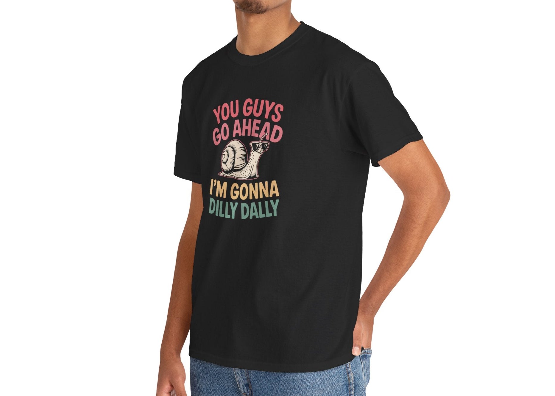 Model wearing a black T-shirt featuring "You Guys Go Ahead, I'm Gonna Dilly Dally" text in a retro 90s-style font with a snail illustration. Part of the Vivid Divergence Sensory Friendly Unisex Tees Range.