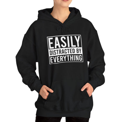 Model wearing a black hoodie with the text "Easily Distracted by Everything" in bold white lettering. Part of the Vivid Divergence Sensory Friendly Unisex Hoodie Range.