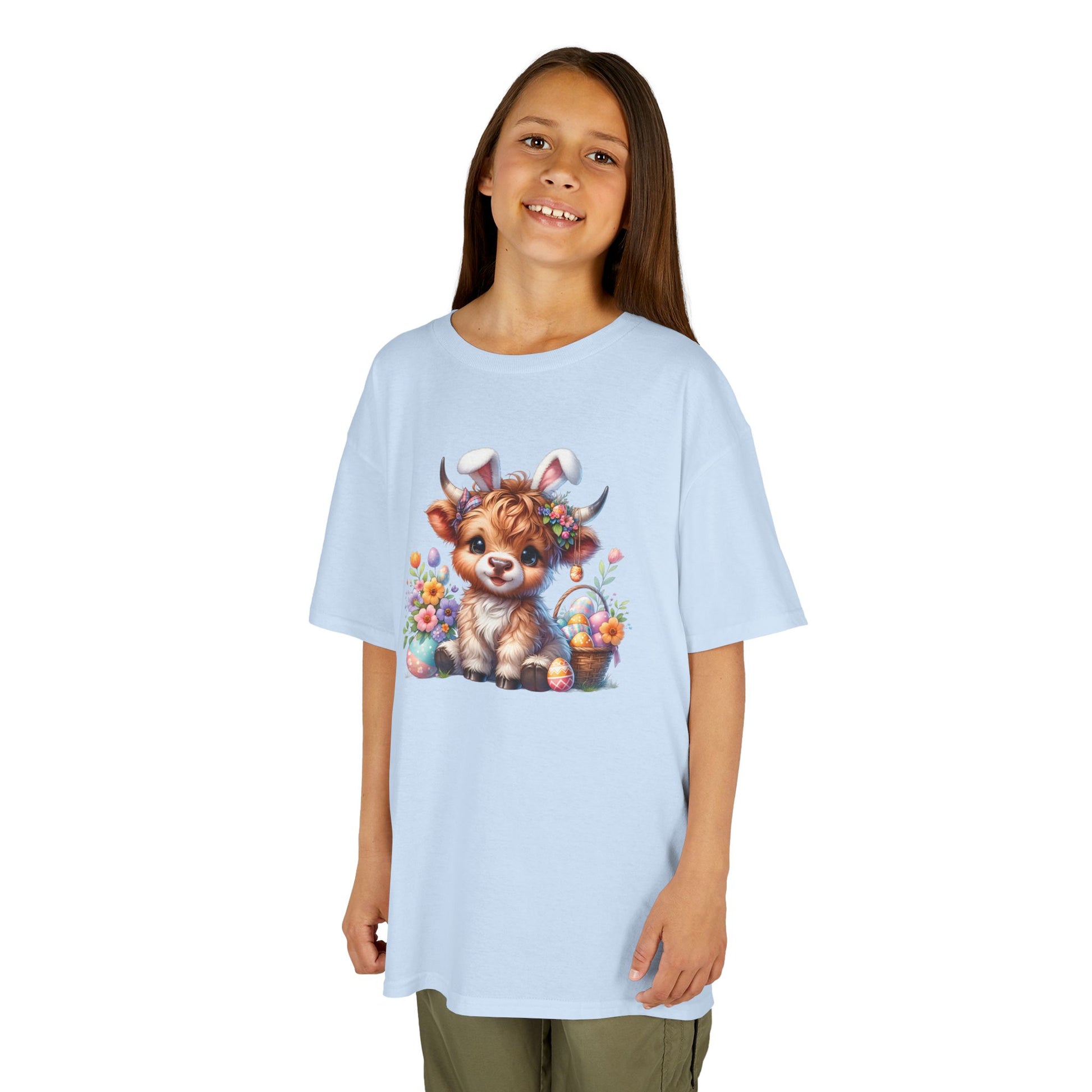 Child wearing a light blue Easter T-shirt featuring a Highland cow, decorated eggs, and floral elements, perfect for spring. Hop into the season in style and shop Easter shirts online today!