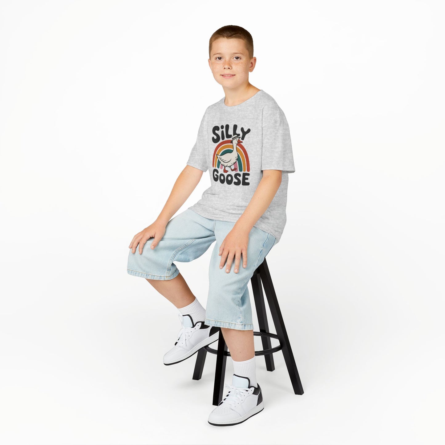 Boy sitting on a stool wearing a gray "Silly Goose" rainbow kids T-shirt with a cartoon goose and colorful rainbow. Part of the Vivid Divergence Sensory Friendly Kids Shirts Range. The perfect T-shirt for sensory-sensitive kids and comes with a Sensory Satisfaction Promise.