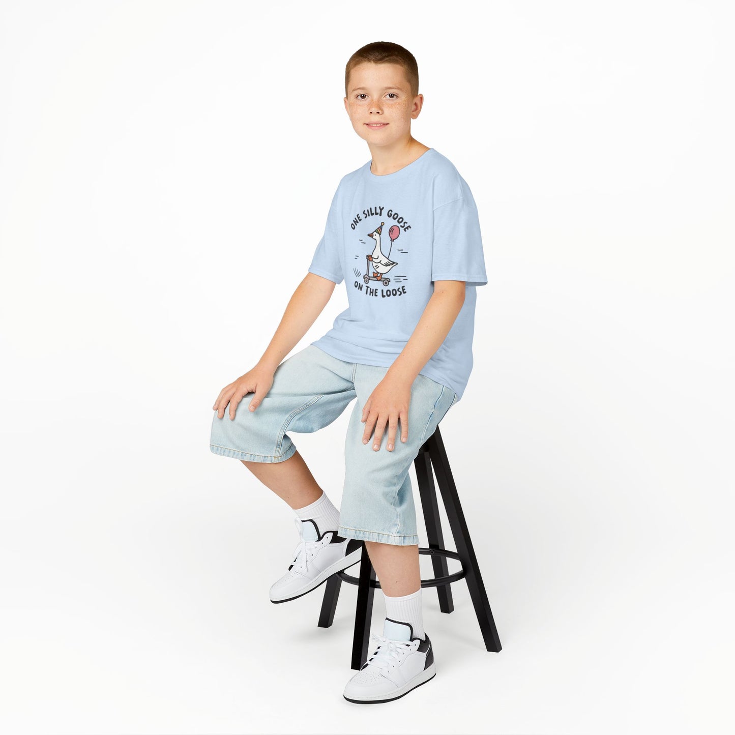 Boy sitting on a stool wearing a light blue "One Silly Goose On The Loose" kids T-shirt with a playful cartoon goose. Part of the Vivid Divergence Sensory Friendly Kids Shirts Range. The perfect T-shirt for sensory-sensitive kids and comes with a Sensory Satisfaction Promise.