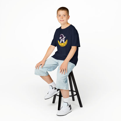 Boy sitting on a stool wearing a navy blue "Dabbing Astronaut on the Moon" kids T-shirt with an astronaut dabbing while sitting on a crescent moon. Part of the Vivid Divergence Sensory Friendly Kids Shirts Range. The perfect T-shirt for sensory-sensitive kids and comes with a Sensory Satisfaction Promise.