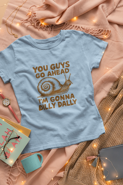 Close-up view of a light blue T-shirt with the text "You Guys Go Ahead, I'm Gonna Dilly Dally" and a playful snail graphic in brown. Part of the Vivid Divergence Sensory Friendly Unisex Tees Range.