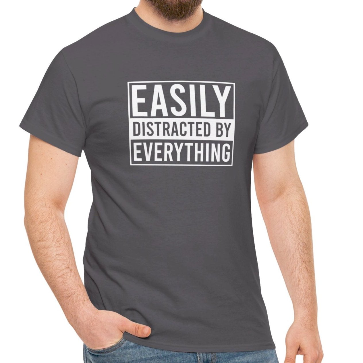 A person wearing a dark gray T-shirt with "Easily Distracted by Everything" text, standing casually. Part of the Vivid Divergence Sensory Friendly Unisex Tees Range.