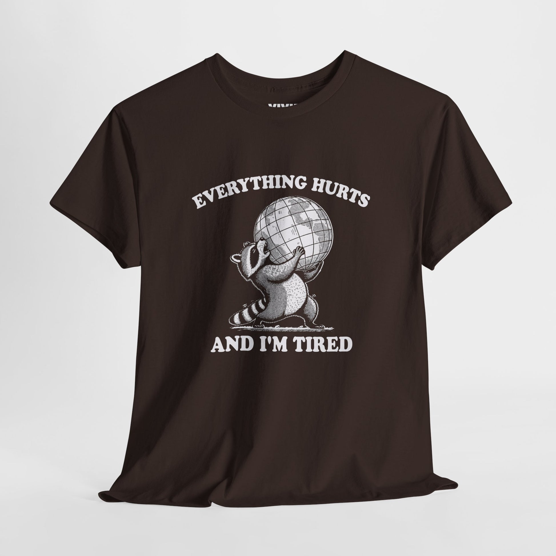 Hanging view of chocolate brown T-shirt featuring a vintage style sketch of a raccoon carrying the world with the phrase “Everything Hurts and I’m Tired.” The official uniform of burnt out. Part of the Vivid Divergence Memewear Collection!