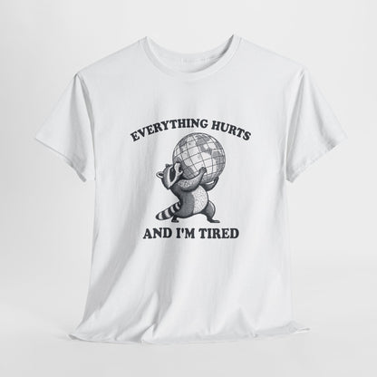 Hanging view of white T-shirt featuring a vintage style sketch of a raccoon carrying the world with the phrase “Everything Hurts and I’m Tired.” The official uniform of burnt out. Part of the Vivid Divergence Memewear Collection!