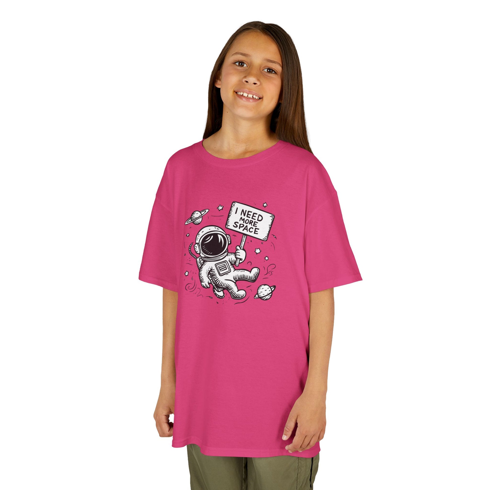 Girl wearing a pink "I Need More Space" astronaut kids T-shirt with a cartoon astronaut floating among space icons. Part of the Vivid Divergence Sensory Friendly Kids Shirts Range. The perfect T-shirt for sensory-sensitive kids and comes with a Sensory Satisfaction Promise.