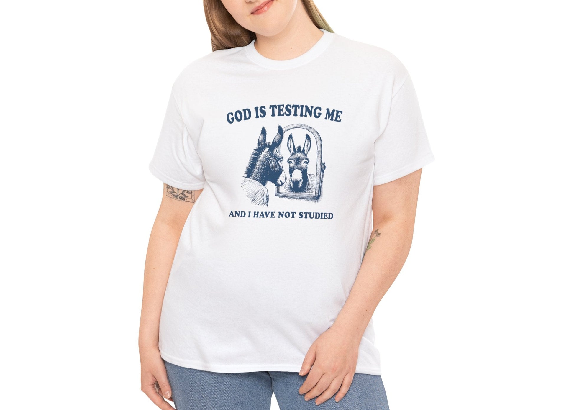Modeled view of white T-shirt with vintage-style illustration of a distressed donkey and the phrase “God is testing me and I have not studied.” Divine pressure, zero preparation. Part of the Vivid Divergence Memewear Collection!