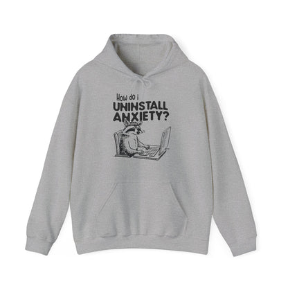 Front view of a gray hoodie featuring the text "How Do I Uninstall Anxiety?" and a cartoon illustration of a raccoon using a laptop. Part of the Vivid Divergence Sensory Friendly Unisex Hoodie Range.