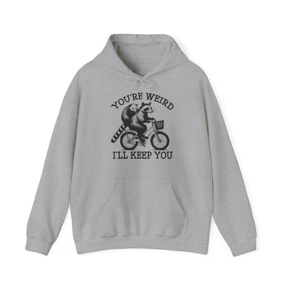 Front view of a gray hoodie featuring the text "You're Weird, I'll Keep You" with a cartoon illustration of two raccoons riding a bicycle. Part of the Vivid Divergence Sensory Friendly Unisex Hoodie Range.