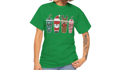 Model wearing a green T-shirt featuring a festive illustration of four iced coffee cups decorated with Christmas designs, styled in a cozy indoor setting. Part of the Vivid Divergence Sensory Friendly Unisex.