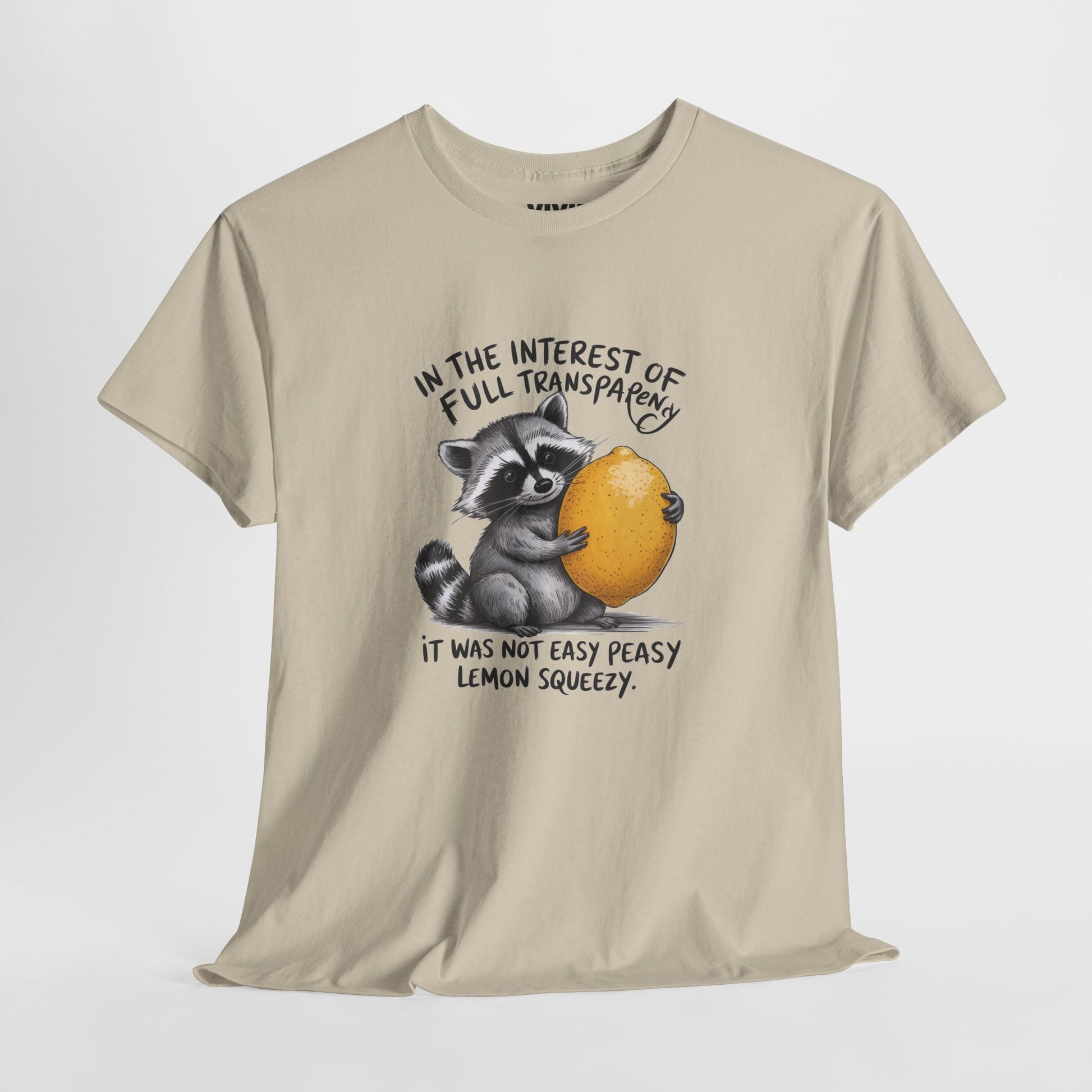 Hanging view of beige T-shirt featuring a raccoon holding onto a lemon with the text “In the interest of transparency, it was not easy peasy lemon squeezy.” The emotional squeeze is real. Part of the Vivid Divergence Memewear Collection!